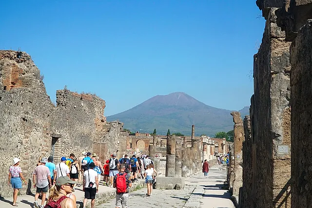Visitors walking along the street into the Forum of Pompeii with Mount Vesuvius in the distance